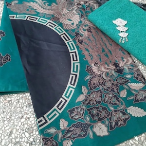 Puede incluir: Vista aérea de tres piezas de tela estampada. La más grande es de color verde azulado con un semicírculo negro y un borde geométrico. Las otras piezas son de color verde azulado con diseños florales y de pájaros. Una broche plateada está en una pieza.