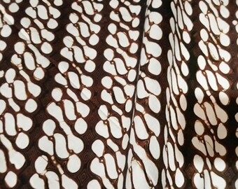 Könnte beinhalten: Weißer Stoff mit einem braunen Batik-Muster aus sich wiederholenden Tropfenformen.