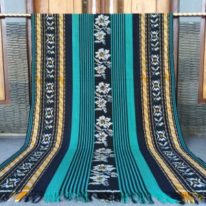 Könnte beinhalten: Ein gewebtes Stofftextil mit einem gestreiften Muster in Schwarz, Türkis und Gold. Der Stoff hat einen Fransenrand und ein florales Design.