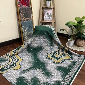 Puede incluir: Tela verde con un patrón abstracto blanco y dorado. La tela tiene un borde blanco con un diseño geométrico.
