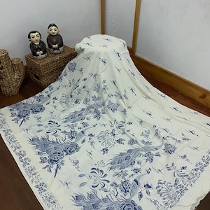Puede incluir: Tela blanca con un diseño de pavo real azul y blanco. La tela está doblada y drapeada sobre una superficie de madera.