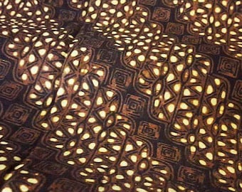 Könnte beinhalten: Nahaufnahme eines braunen Stoffes mit einem sich wiederholenden Muster aus hellbraunen und weißen geometrischen Formen. Der Stoff hat eine strukturierte Oberfläche und ein leicht verblichenes Aussehen.