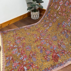 Puede incluir: Una tela de color amarillo mostaza con un patrón floral en tonos de rosa, azul y rojo. La tela tiene un brillo sutil y una textura suave.