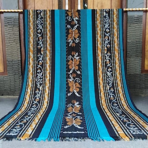 May include: A woven throw blanket with a black, blue, and gold striped pattern. The blanket has a traditional ikat design with floral motifs.