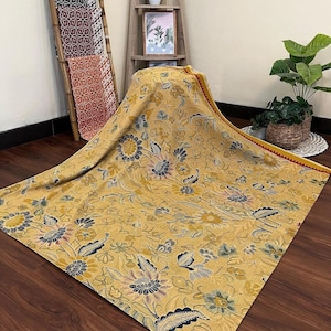 May include: A yellow and blue floral patterned throw blanket with a red and yellow border. The blanket is folded and draped over a wooden shelf.