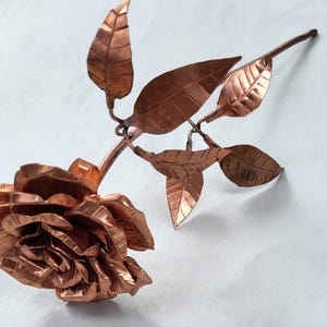 May include: A copper rose with leaves, crafted from metal. The rose is made of many overlapping petals, giving it a realistic look.