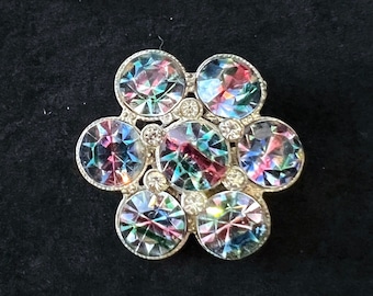 May include: A silver brooch with a flower design featuring iridescent round stones in shades of blue, green, and pink.