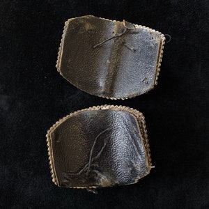 May include: Two black leather patches with silver beading around the edges. The patches are worn and have loose threads.