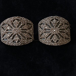 May include: Two silver-toned metal embellishments with a starburst design. The embellishments are made of small, round beads.