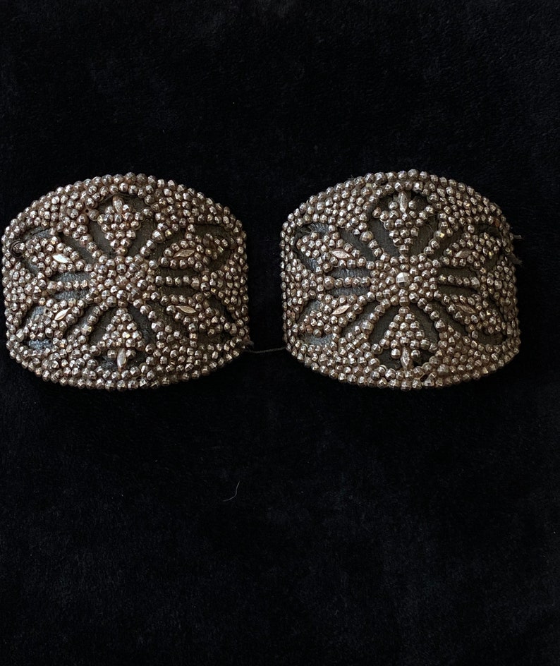 May include: Two silver-toned metal embellishments with a starburst design. The embellishments are made of small, round beads.