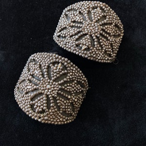 May include: Two silver metal decorative embellishments with a starburst design. The embellishments are made of small, round beads.