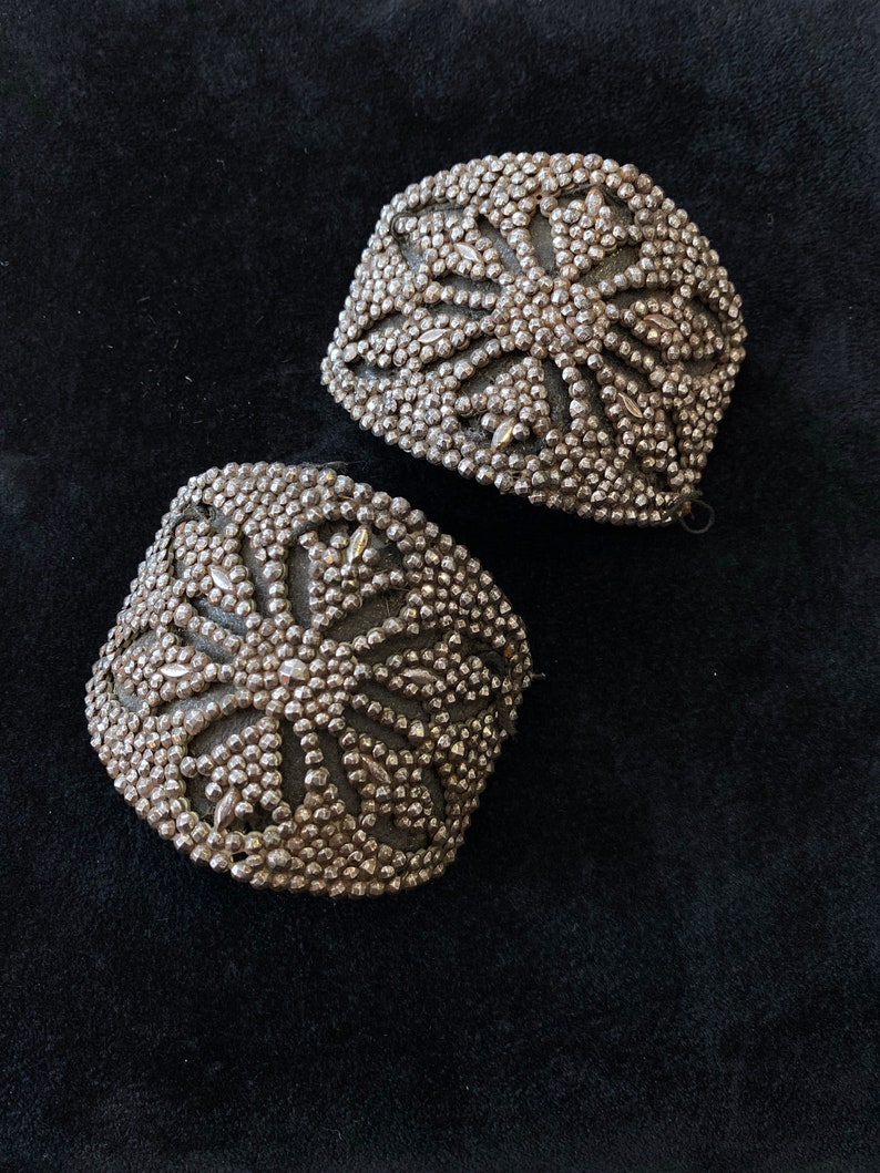 May include: Two silver metal decorative embellishments with a starburst design. The embellishments are made of small, round beads.