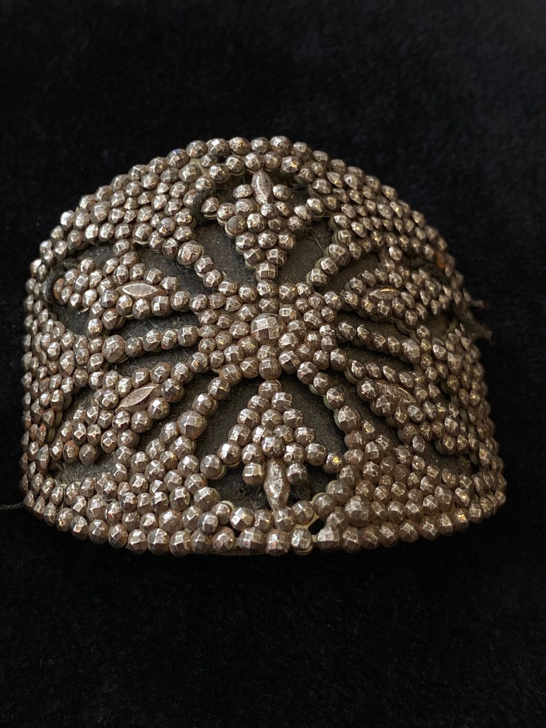May include: A silver-toned metal bracelet with a decorative design of small, raised circles and a starburst pattern.
