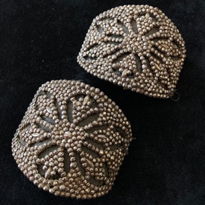 May include: Two silver metal embellishments with a starburst design. The embellishments are made of small, round beads.