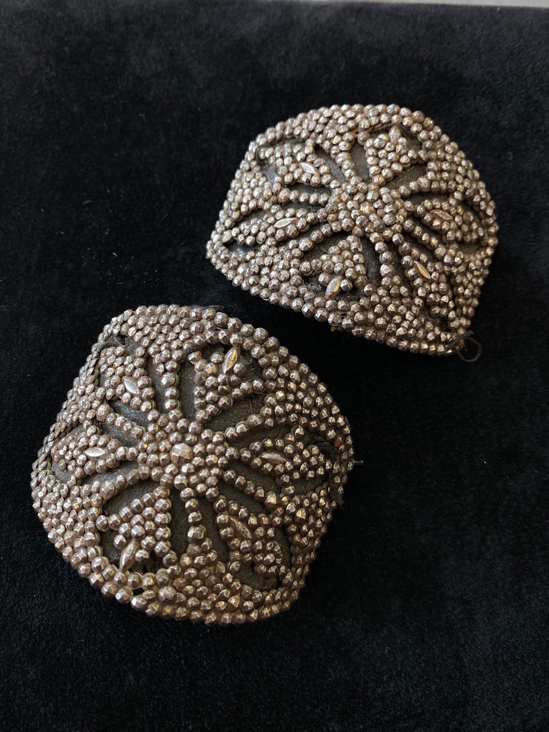 May include: Two silver metal embellishments with a starburst design. The embellishments are made of small, round beads.
