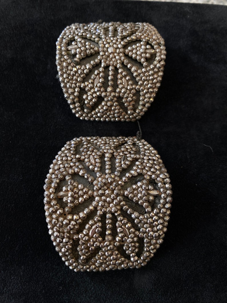 May include: Two silver-toned metal embellishments with a circular design of raised dots and a starburst pattern.