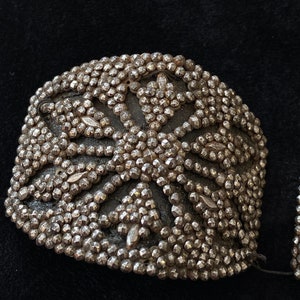 May include: A pair of silver-toned metal embellishments with a geometric design. The embellishments are made of small, round beads that are arranged in a pattern of overlapping circles.