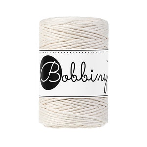 May include: A spool of natural colored cotton cord with a white label that says "Bobbiny" in black cursive lettering.