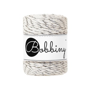 May include: A spool of white twine with silver metallic thread running through it. The spool is labeled "Bobbiny".