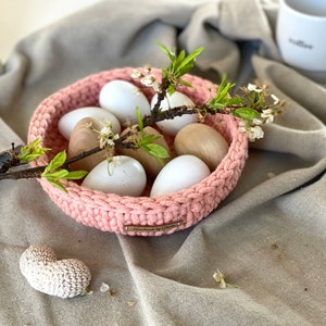 May include: A pink crocheted bowl filled with white and wooden eggs, decorated with a sprig of white blossoms and a wooden tag that reads "Handmade by Danielle".