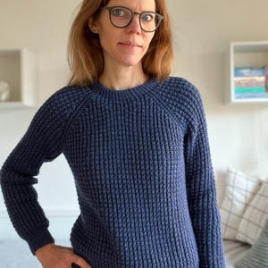 May include: A woman wearing a blue waffle knit sweater with long sleeves and a round neckline.