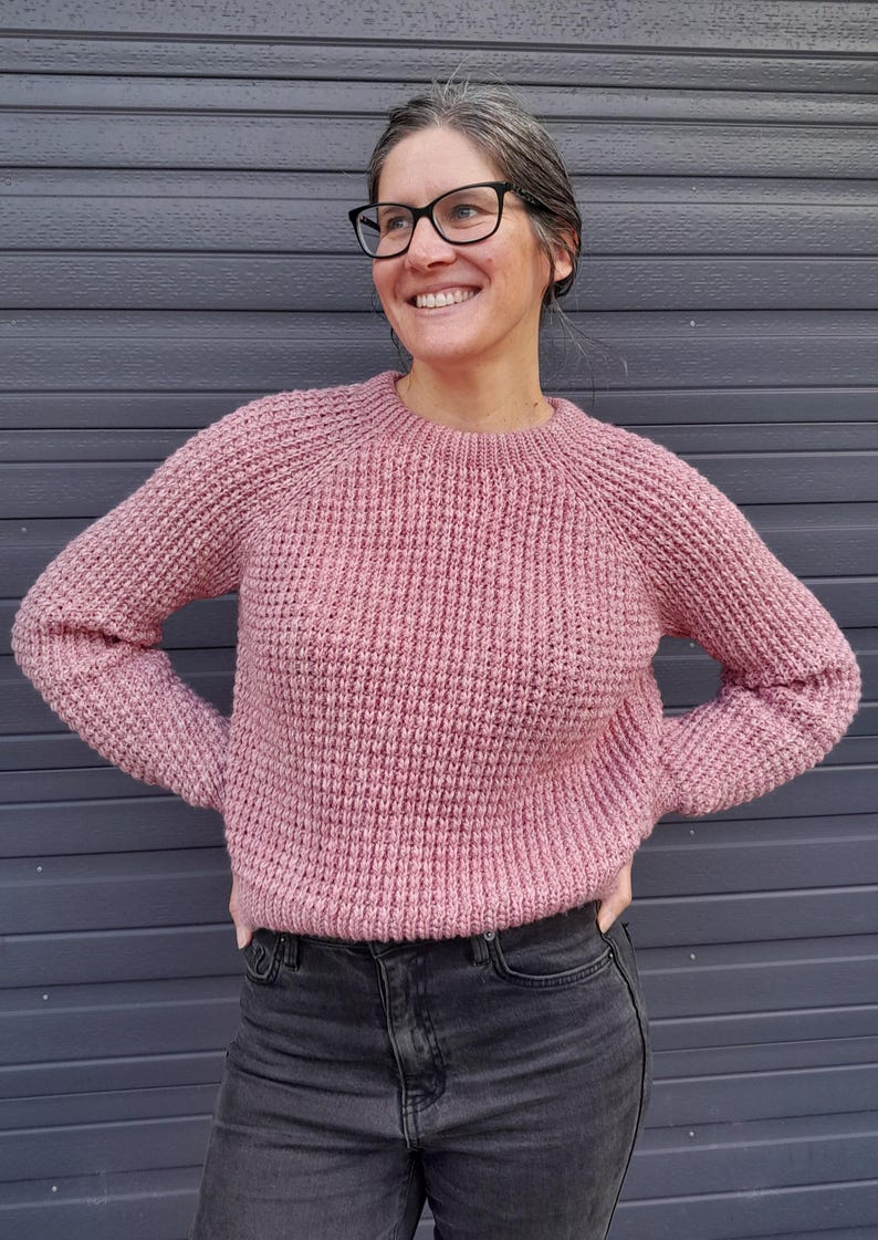 May include: A pink knitted sweater with a round neckline and long sleeves. The sweater has a waffle knit texture.