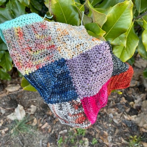 May include: A multi-colored crocheted blanket with squares in shades of blue, pink, green, brown, and grey.