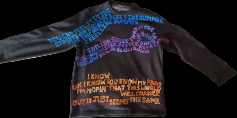 Pode incluir: Uma camisa preta de manga comprida com texto colorido estampado na frente. O texto diz "You can feel it in the streets on a day like this, the heat it feel like summer, I feel like summer, 7 billion souls that move around the sun, rolling faster, faster, and not a chance to slow down, slow down. I know, oh, I know you know my pain, I'm hopin' that this world will change, but it just seems the same."