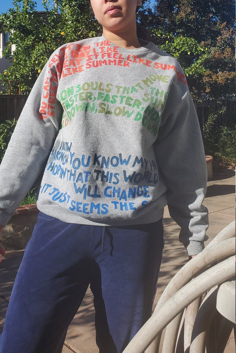 Pode incluir: Camisola de moletom cinza com texto colorido que diz "The day it feel like summer on souls that move faster, faster, and down, slow down. I know you know my heart, in that this world will change it just seems the..."