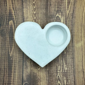 May include: A white heart-shaped ceramic dish with a small round indentation in the center. The dish is perfect for holding small items like jewelry or candles.