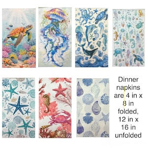 May include: A collection of seven rectangular dinner napkins featuring various marine life illustrations including sea turtles, jellyfish, whales, crabs, and seashells. The text states: Dinner napkins are 4 in x 8 in folded, 12 in x 16 in unfolded.