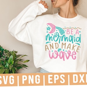 May include: White sweatshirt with a teal and pink mermaid design and the text "Be a mermaid and make wave".
