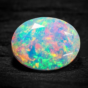 May include: A white opal gemstone with iridescent colours of green, blue, pink, and orange. The opal is oval shaped and has a smooth, polished surface.