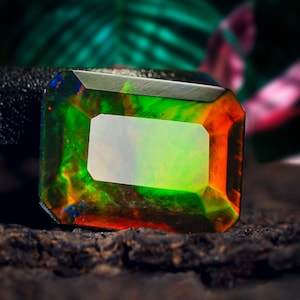 Puede incluir: Una gema rectangular de color verde, naranja y azul vibrante. La gema está tallada y pulida, con una superficie lisa y reflectante.