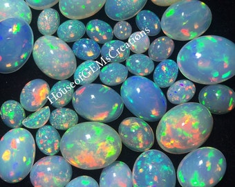 May include: A collection of oval-shaped opal cabochons in various sizes. The opals are a milky white color with iridescent flashes of green, blue, pink, and orange.