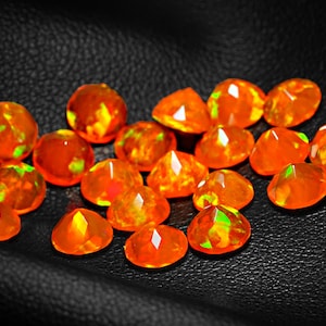 May include: A collection of orange and green fire opals, with a variety of shapes and sizes, displayed on a black leather surface.