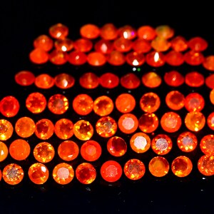 Puede incluir: Una colección de pequeñas opalas redondas de color naranja. Las opalas están dispuestas en forma de semicírculo sobre un fondo negro.