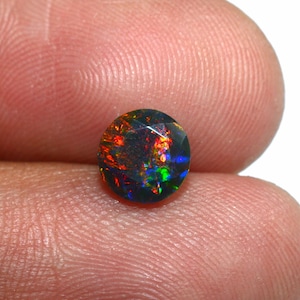 Puede incluir: Una piedra preciosa de ópalo negro redonda con un brillo iridiscente rojo, verde y azul.