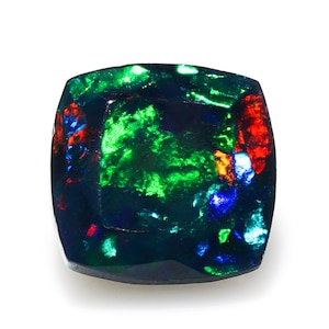 May include: A black opal gemstone with green, blue, and red flashes of colour. The gemstone is cut into a square shape with rounded edges.