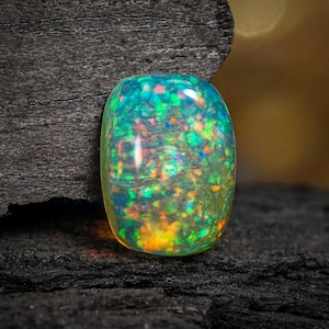 Könnte beinhalten: Ein lebendiger, oval geformter Opal-Edelstein. Der Opal zeigt ein fesselndes Farbspiel mit grünen, blauen, orangen und gelben Blitzen. Der Edelstein ist vor einem dunklen, strukturierten Hintergrund platziert, der seine Brillanz hervorhebt.