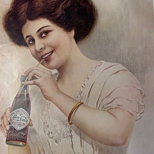 May include: A woman in a white dress with lace trim is drinking from a glass bottle of Coca-Cola. The bottle has a diamond-shaped label with the Coca-Cola logo and the text "Drink Coca-Cola" and "Trade Mark Registered".