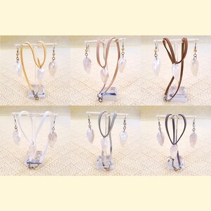 May include: Six sets of iridescent leaf-shaped earrings and necklaces. Each set features a different coloured cord: beige, brown, grey, white, and two shades of brown. The earrings and necklaces are displayed on stands.