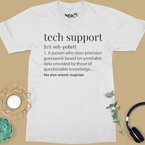 Op de afbeelding: Wit T-shirt met een humoristische definitie van "technische ondersteuning" gedrukt op de voorkant. De definitie luidt: "[tek suh-pohrt] 1. Een persoon die nauwkeurige aannames doet op basis van onbetrouwbare gegevens die worden verstrekt door mensen met twijfelachtige kennis... Zie ook: tovenaar, magiër"