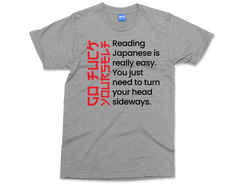 May include: A heather grey t-shirt with a humorous message about reading Japanese. The text reads: "GO チムCケソロムヤラモレチ Reading Japanese is really easy. You just need to turn your head sideways."