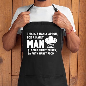 Pu&ograve; includere: Grembiule nero con testo bianco che recita "This is a manly apron, for a manly man doing manly things, with manly food". Il testo &egrave; accompagnato da un cappello da cuoco e un baffo.