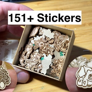 Può includere: Una scatola di legno piena di oltre 151 adesivi Pokemon. Gli adesivi sono in legno e presentano diversi personaggi Pokemon. La scatola è aperta e gli adesivi sono visibili. Il testo "151+ Stickers" è scritto nella parte superiore dell'immagine.