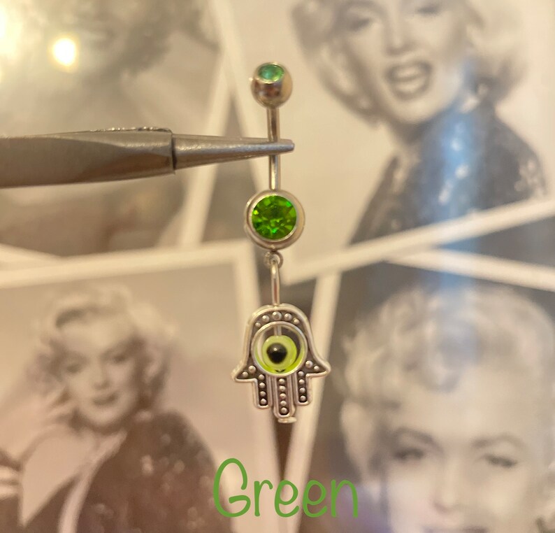 May include: A silver belly button ring with a green gemstone and a Hamsa hand charm with an evil eye design. The word "Green" is written in a green script font at the bottom of the image.