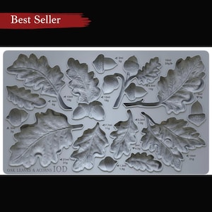 May include: A grey silicone mould featuring detailed oak leaves and acorns. The mould includes various sizes of leaves and acorns, with measurements in millilitres and grams. The text "OAK LEAVES & ACORNS IOD" is printed at the bottom. The words "Best Seller" are at the top.
