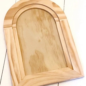 May include: An unfinished wooden arched frame in a light colour. The frame has a rectangular base with an arched top. The wood grain is visible. The frame is likely for a mirror or artwork, measuring approximately 30 cm in height.