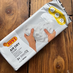 May include: A packet of Jovi Air Dry Clay in Pure White. The packaging shows a hand holding a portion of the white clay. The packet also includes the text "Air dry clay", "3+", and "Recommended by Educators".